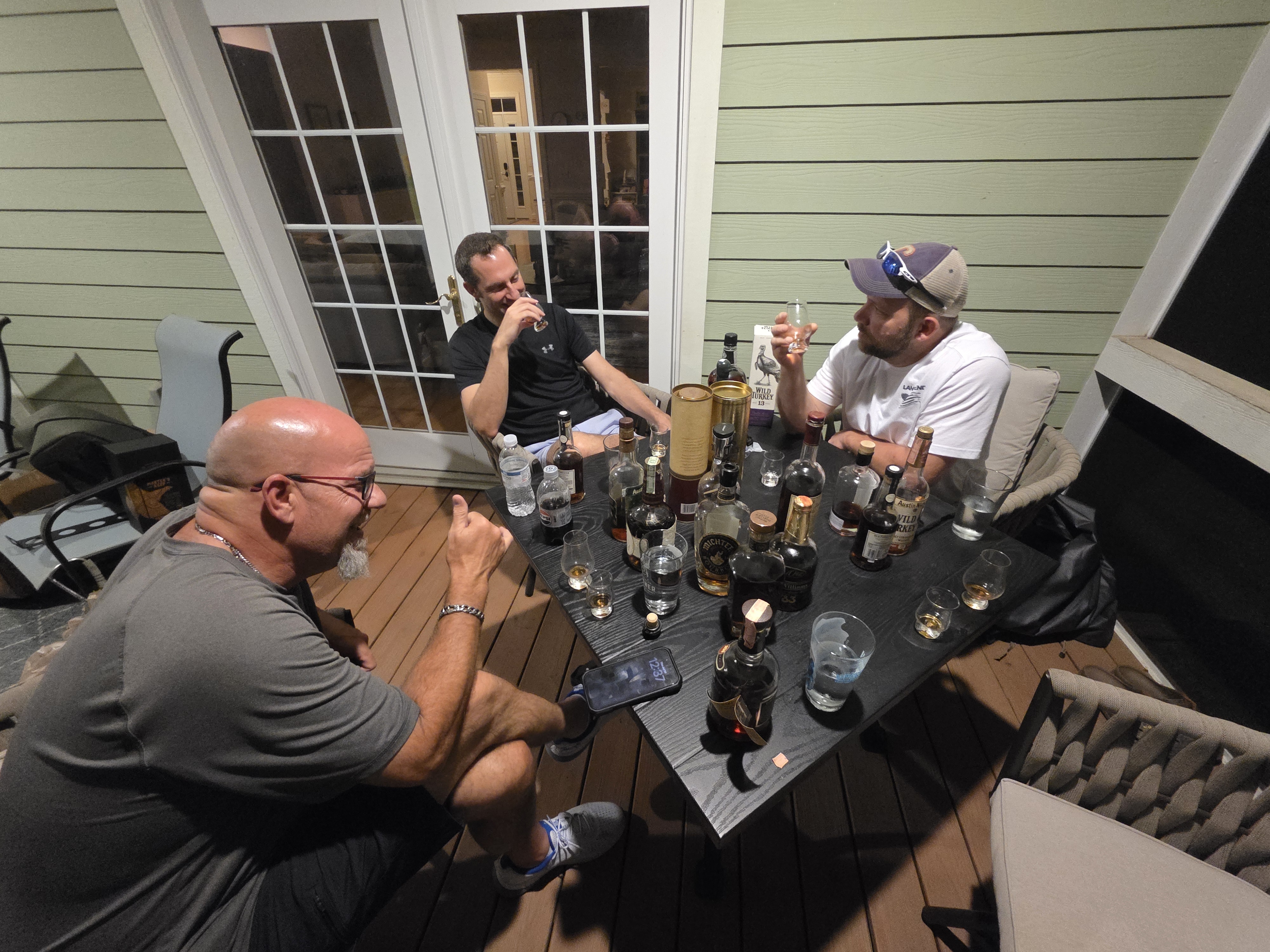 Three dudes around a deck table late on Dan's birthday night, glasses up and bottles stacked between them.