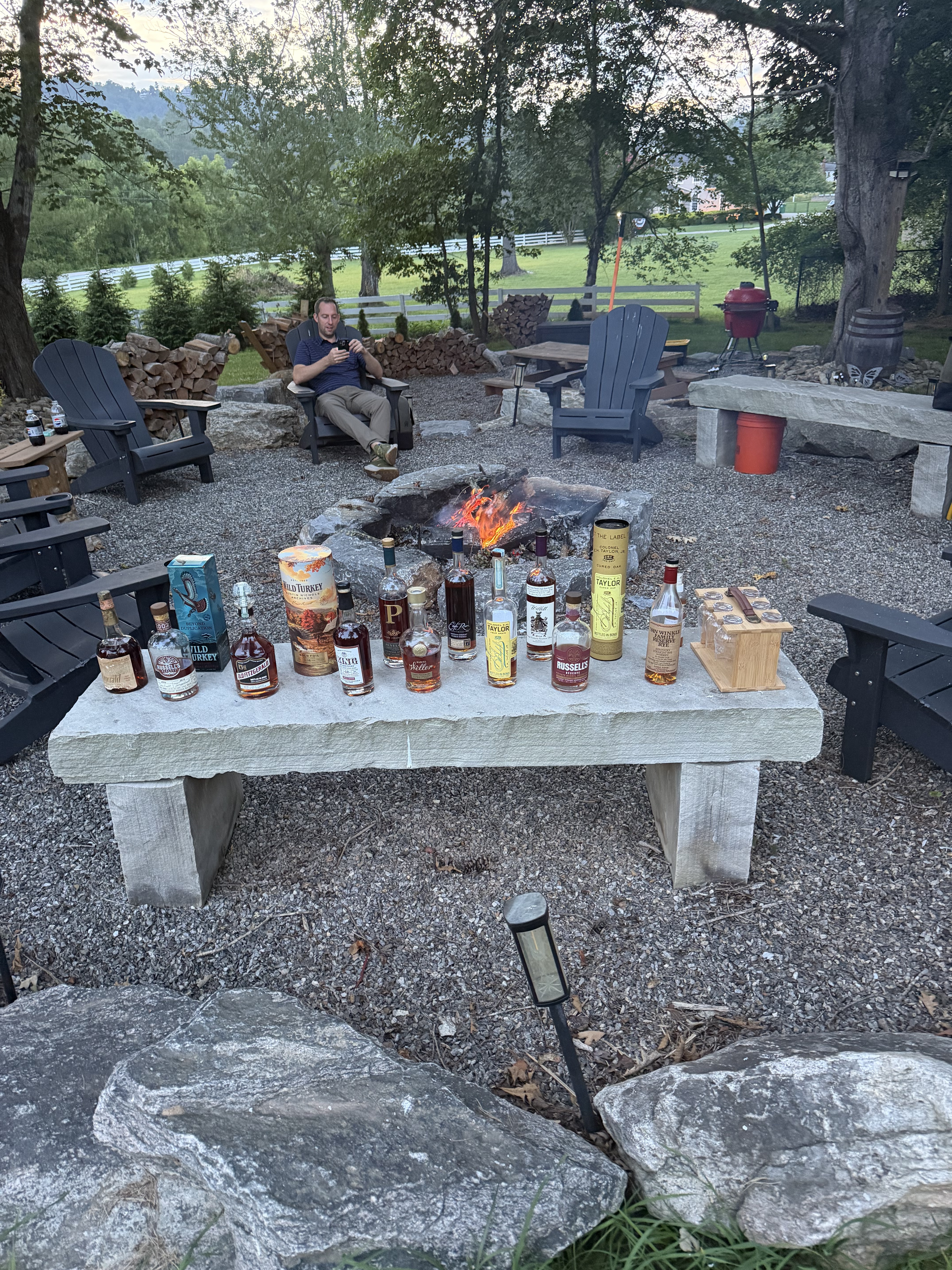 Bourbon bottles lined on a stone bench beside a burning fire pit.
