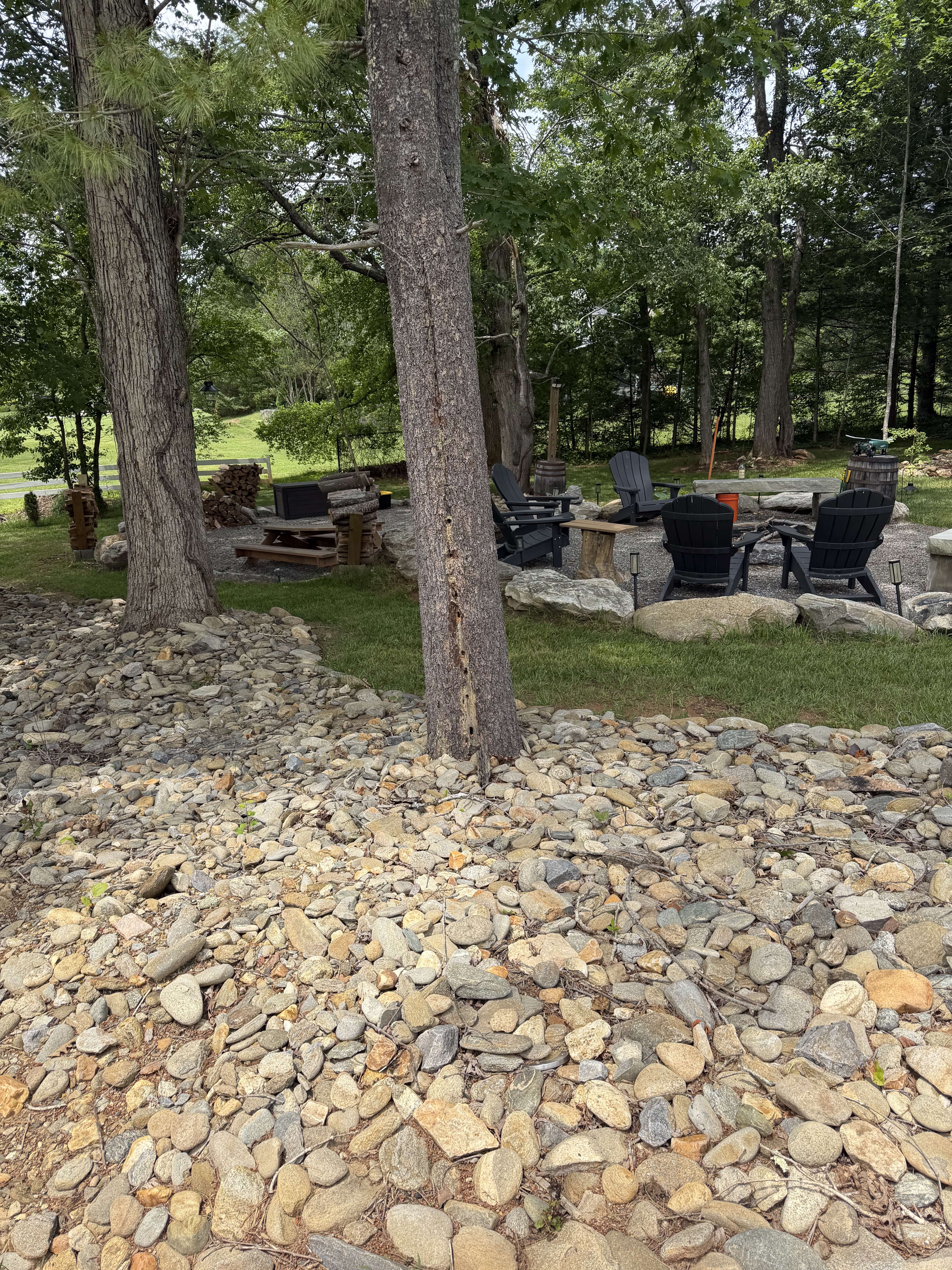 Empty Adirondack chairs arranged around the gravel fire pit.